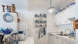 Una cocina con armarios blancos, vajilla de cerámica azul y blanca, un reloj y una lámpara colgante.