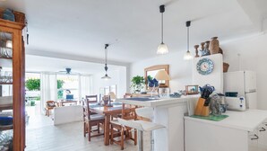 Una cocina moderna con armarios blancos, un comedor con sillas de madera e iluminación colgante.