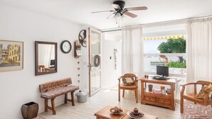 Una habitación con un banco de madera, una mesa con un cuenco de fruta, un televisor y vistas al exterior.