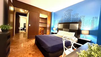 Una habitación de hotel moderna con una cama grande, un armario empotrado, una zona de estar con mesa y un mural de la ciudad en la pared.