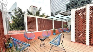 A rooftop terrace with wooden flooring, blue wireframe chairs, and a red lattice fence. - RMS Suites - Zona Rosa (Mexico City)