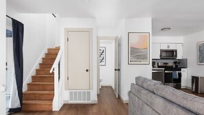 A modern apartment with a staircase, a living area with a sofa, a kitchen with appliances, and artwork on the walls. - Rare 2BR in Prime Location (Austin)