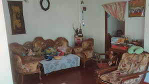 Un salon comprenant un ensemble de canapés, une chaise en bois, une petite table recouverte d’une nappe en dentelle et un coussin rouge sur la chaise.