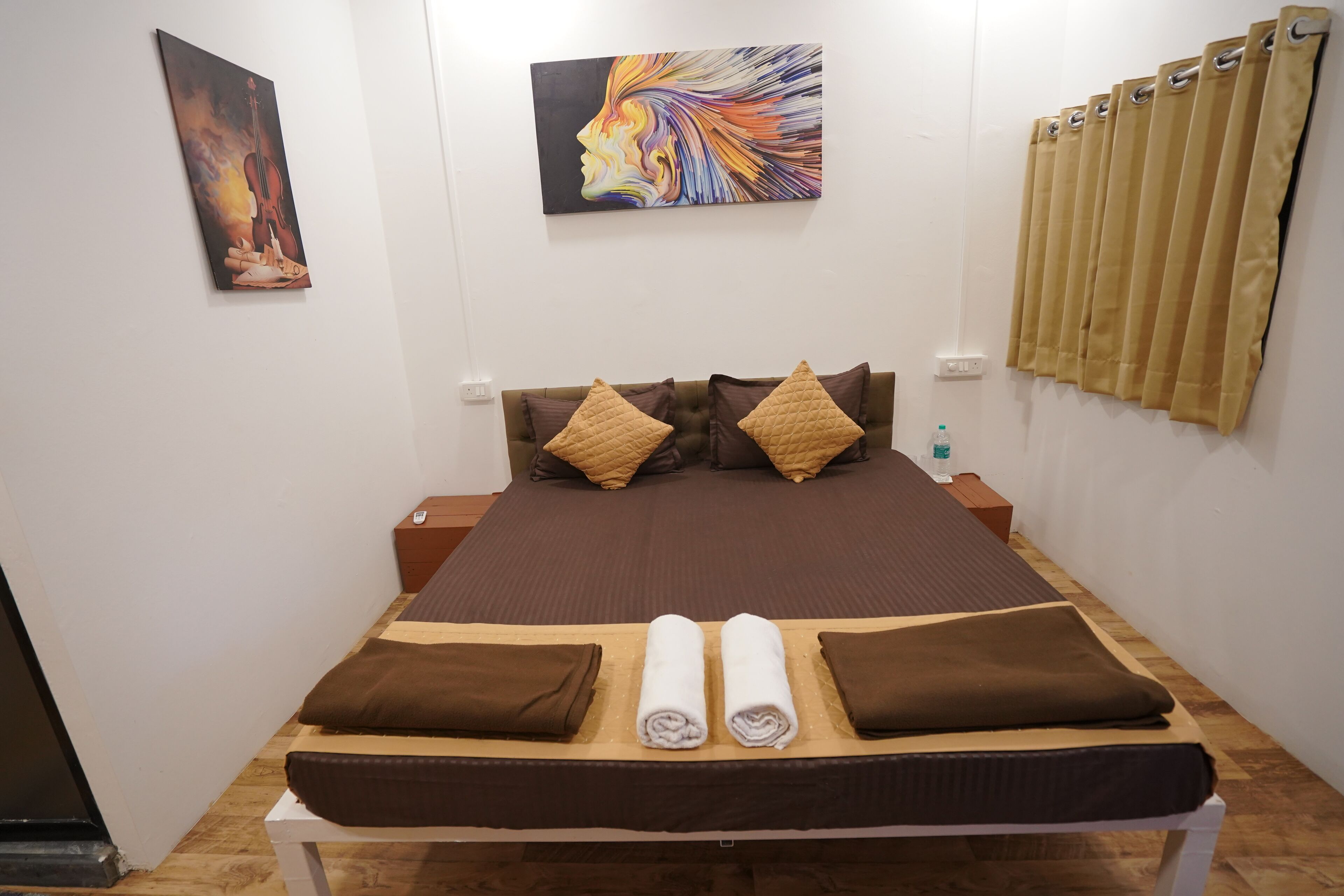A neatly made bed with brown bedding, a headboard with decorative pillows, and two paintings on the wall.