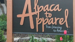 Une enseigne pour « Alpaca to Apparel », avec un arbre et des fleurs en arrière-plan.