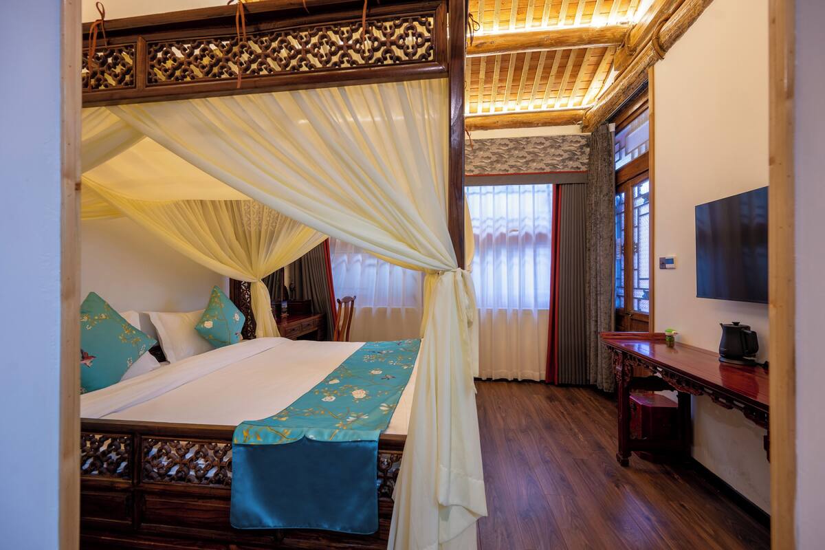Quarto tradicional com cama de dossel, móveis de madeira e televisão na parede.