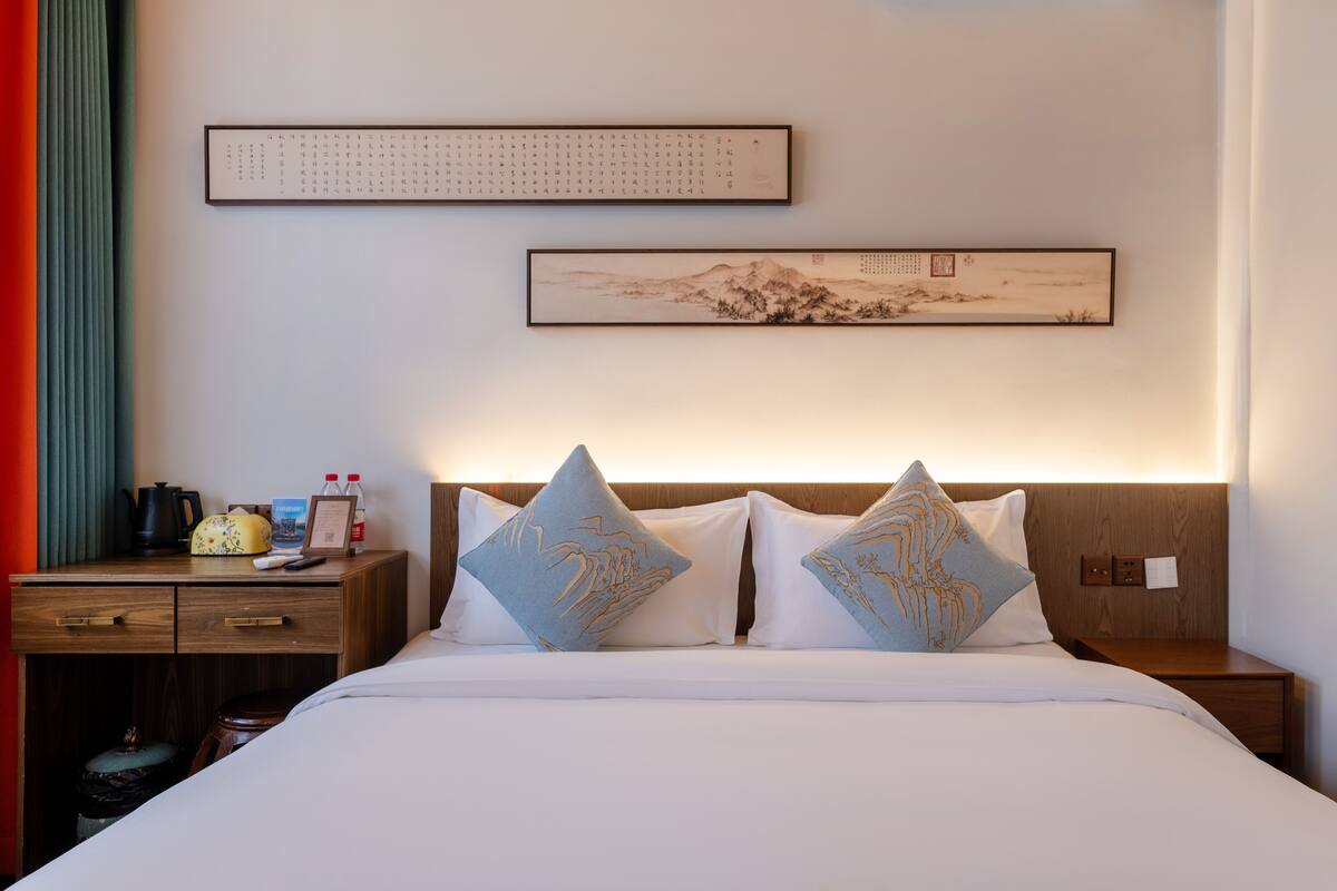 Quarto de hotel bem arrumado com cama, mesas de cabeceira e uma obra de arte na parede.