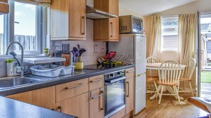 Cocina compacta con armarios de madera, horno integrado y microondas. Cuenta con una zona de comedor con mesa y sillas.