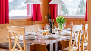 A wooden dining table with white plates, wine glasses, and a bottle of wine, set in a room with red curtains and wooden walls.