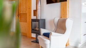 A room with a white chair, a fireplace, a television, and wooden walls.