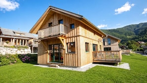 A wooden chalet with a balcony, a stone foundation, and a view of mountains.
