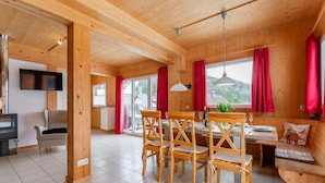 A wooden cabin interior with a dining area, a sofa, a TV, and a fireplace.