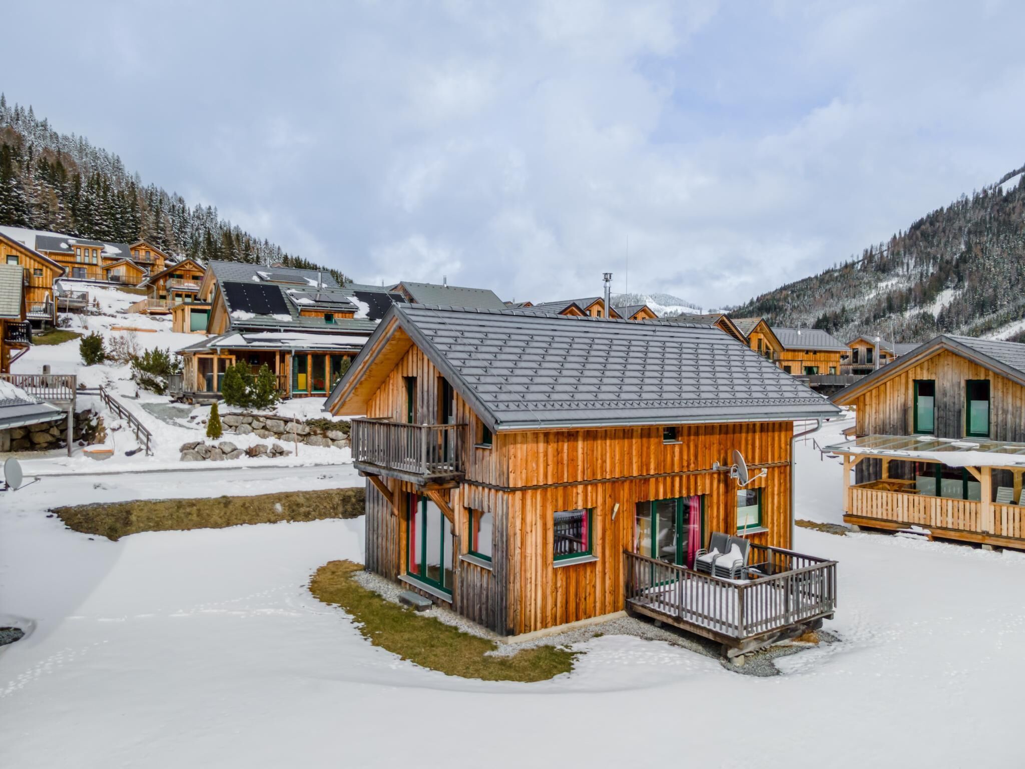 A wooden cabin with a balcony, surrounded by snow-covered ground and mountains.