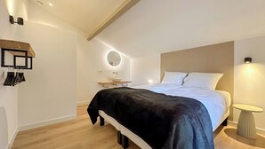 A modern bedroom with a large bed, a bedside table, a round mirror, and a small table with a lamp.
