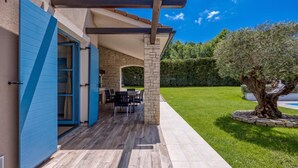 A covered outdoor patio with a dining area, stone wall, and a well-maintained lawn. - Villa Milo Mali Vareski With Pool (Marcana)
