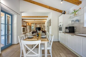 A modern kitchen with white cabinets, a wooden ceiling, and a dining area with white chairs and a wooden table. - Villa Milo Mali Vareski With Pool (Marcana)