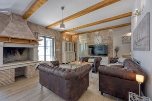 Una sala de estar con chimenea, vigas de madera, televisor y sofás de cuero.