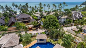 A resort with multiple bungalow-style buildings, a central swimming pool, and a view of the ocean.