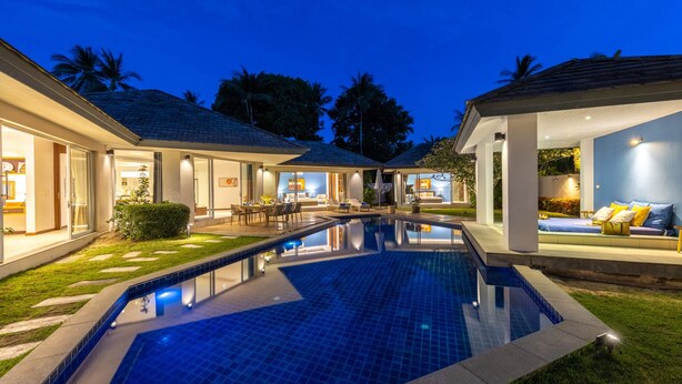 A modern resort with a swimming pool, outdoor seating, and well-lit rooms.