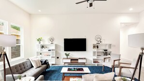 A modern living room with a sofa, coffee table, and TV. There are white shelves with decorative items and a ceiling fan. - Luminous and Cozy 3BR 2Bath Escape (Lexington)