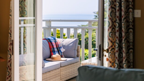 Ein Balkon mit einer Korbus-Couch, einem Hut und einer bunten Decke.
