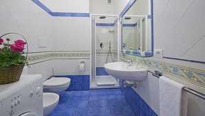 Un baño con ducha, inodoro y lavamanos, con azulejos azules y blancos.