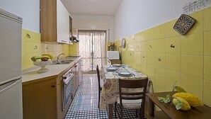 Una cocina compacta con baldosas amarillas, una mesa para dos personas dispuesta y un refrigerador.
