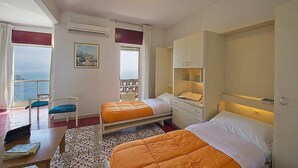Habitación de hotel con dos camas, un escritorio, una silla y vista al mar.