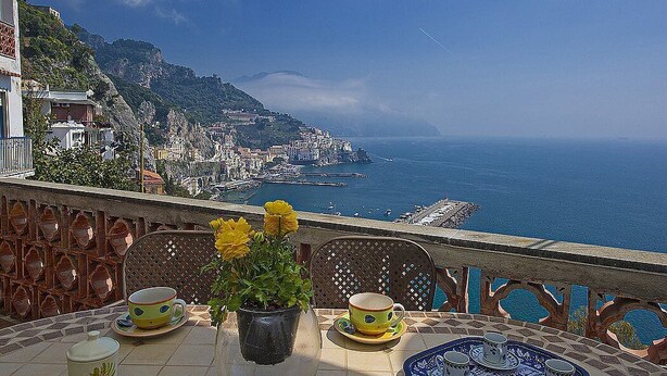 Una terraza con una mesa lista para el té, con vista a un pueblo costero y al mar.