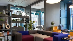 Eine moderne Lounge-Ecke mit einem Ecksofa, einem kleinen Tisch und einem Bücherregal mit Pflanzen.