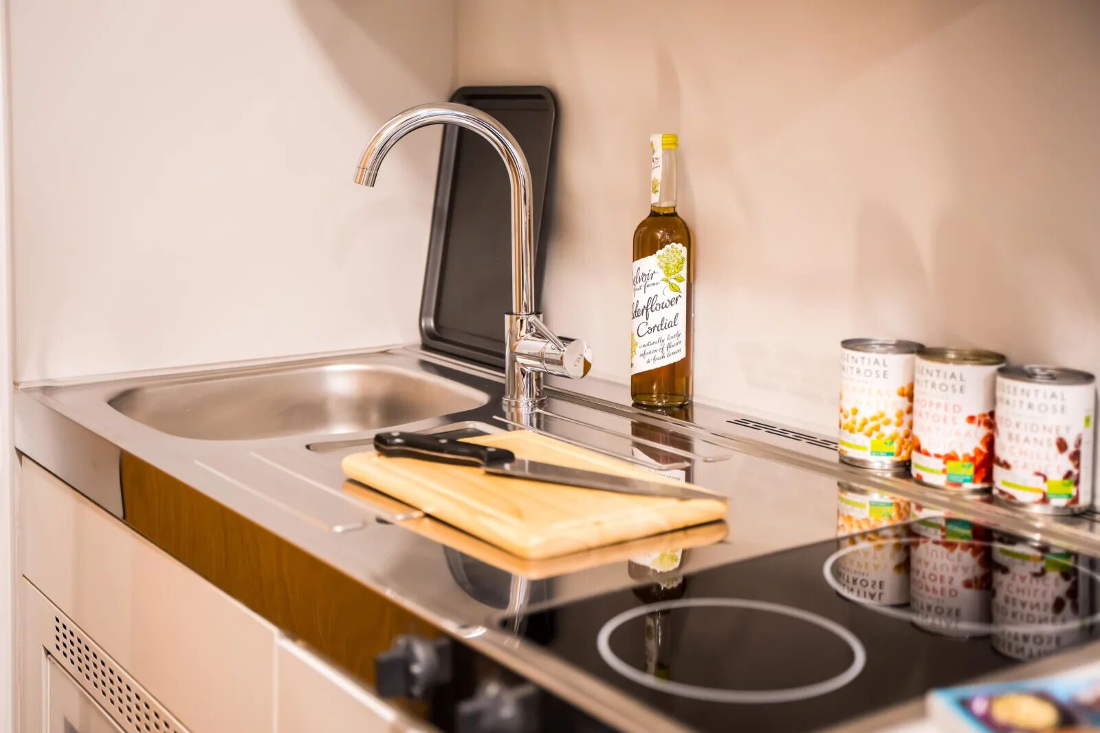 A modern kitchen with a stainless steel sink, a bottle of wine, and canned goods on the counter.