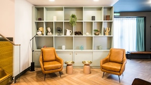 Eine moderne Lobby mit zwei Ledersesseln, einem niedrigen Holzeingangsbereich und einer weißen Regaleinrichtung mit verschiedenen Dekorationsobjekten.