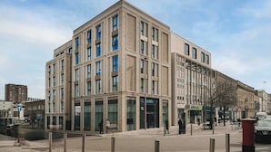 Ein modernes Gebäude mit mehreren Etagen, großen Fenstern und einer Fassade aus Backstein und Glas.