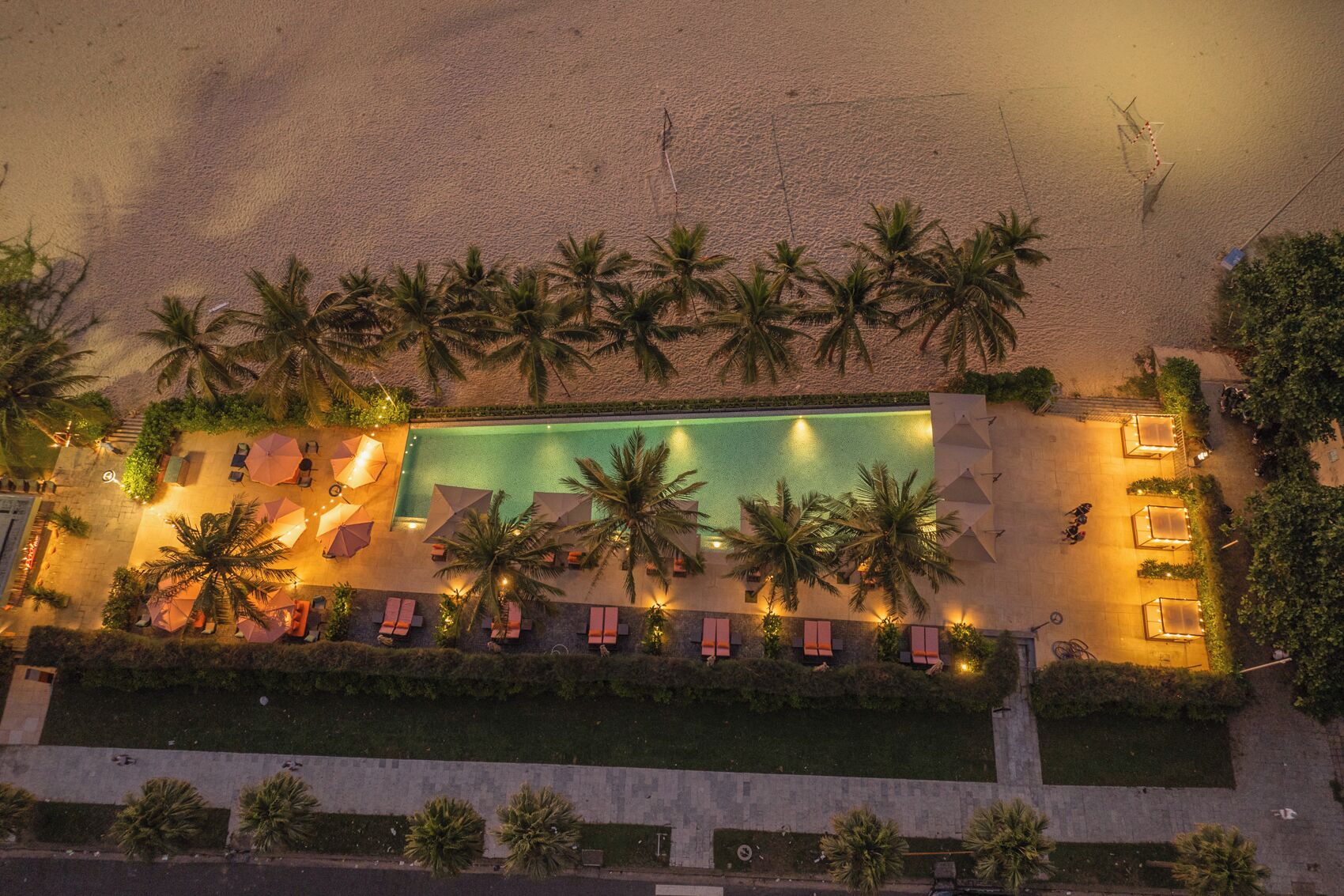 Vista aérea de un resort con piscina rodeada de palmeras y sillas de descanso.
