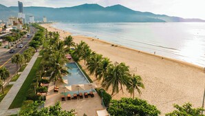 Un resort en la playa con piscina, palmeras y vistas al océano y a las montañas.