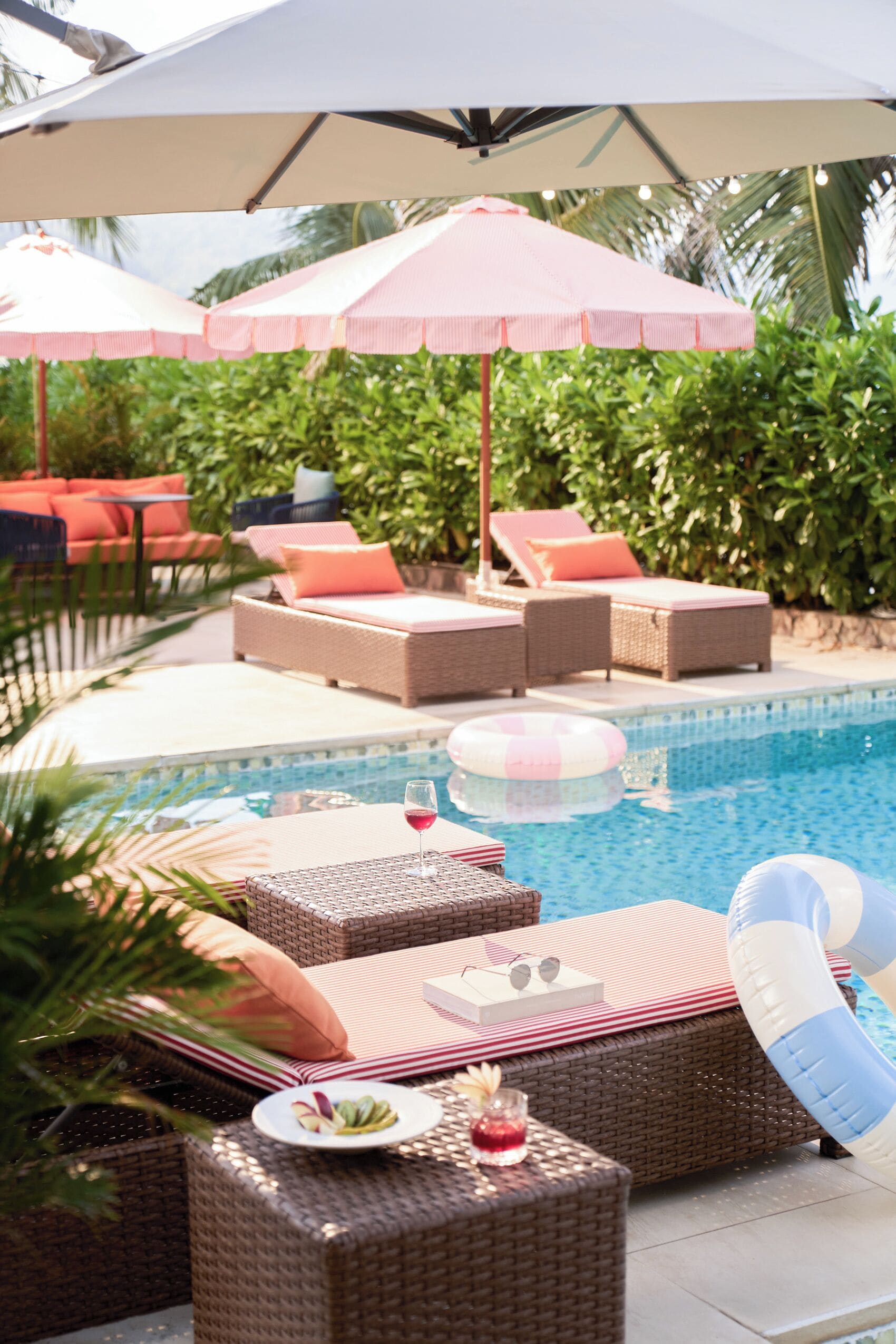 Un espace aménagé au bord de la piscine, avec des fauteuils de relaxation en osier, une piscine et des parasols.