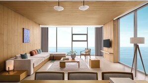 Una sala de estar moderna con un ventanal grande con vistas al mar, un conjunto de sofás, una mesa de centro y un comedor.