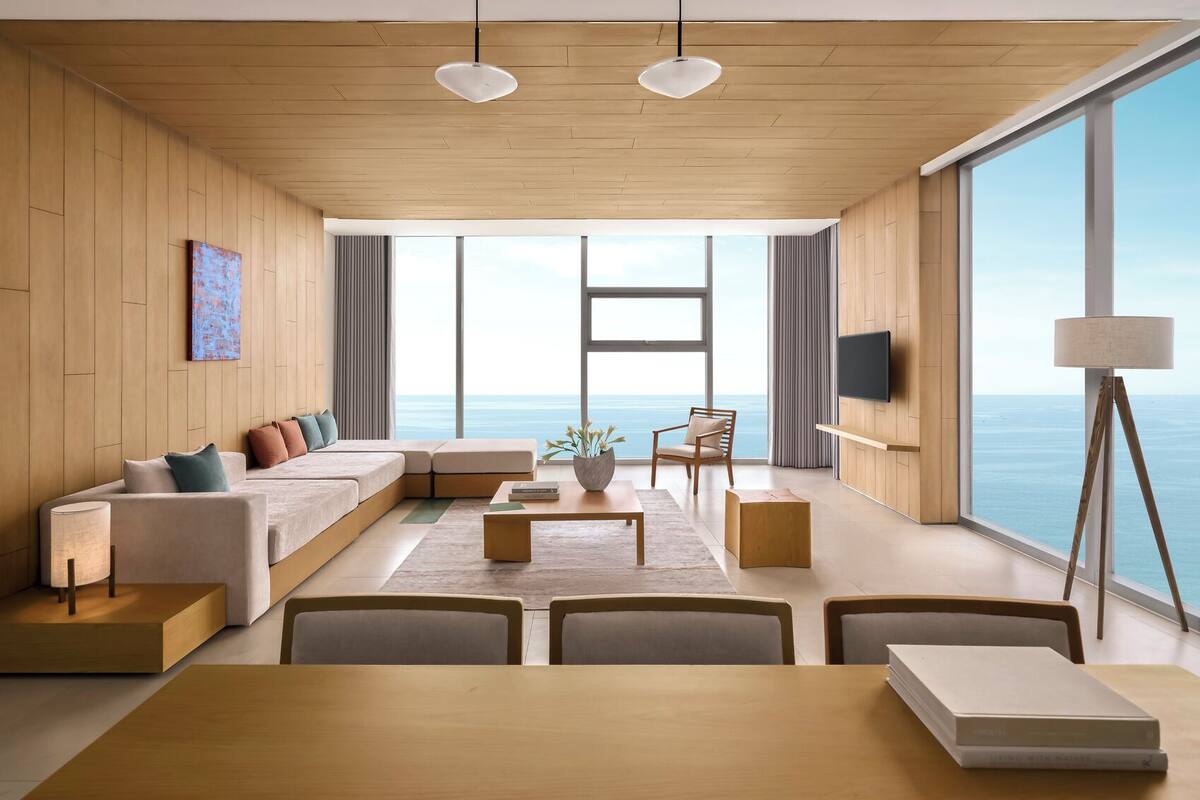 A modern living room with a large window overlooking the sea, a sofa set, a coffee table, and a dining area.