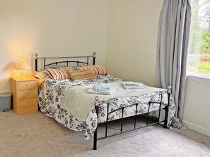 Cama bem arrumada com roupa de cama florida, luminária de cabeceira e janela com cortinas.