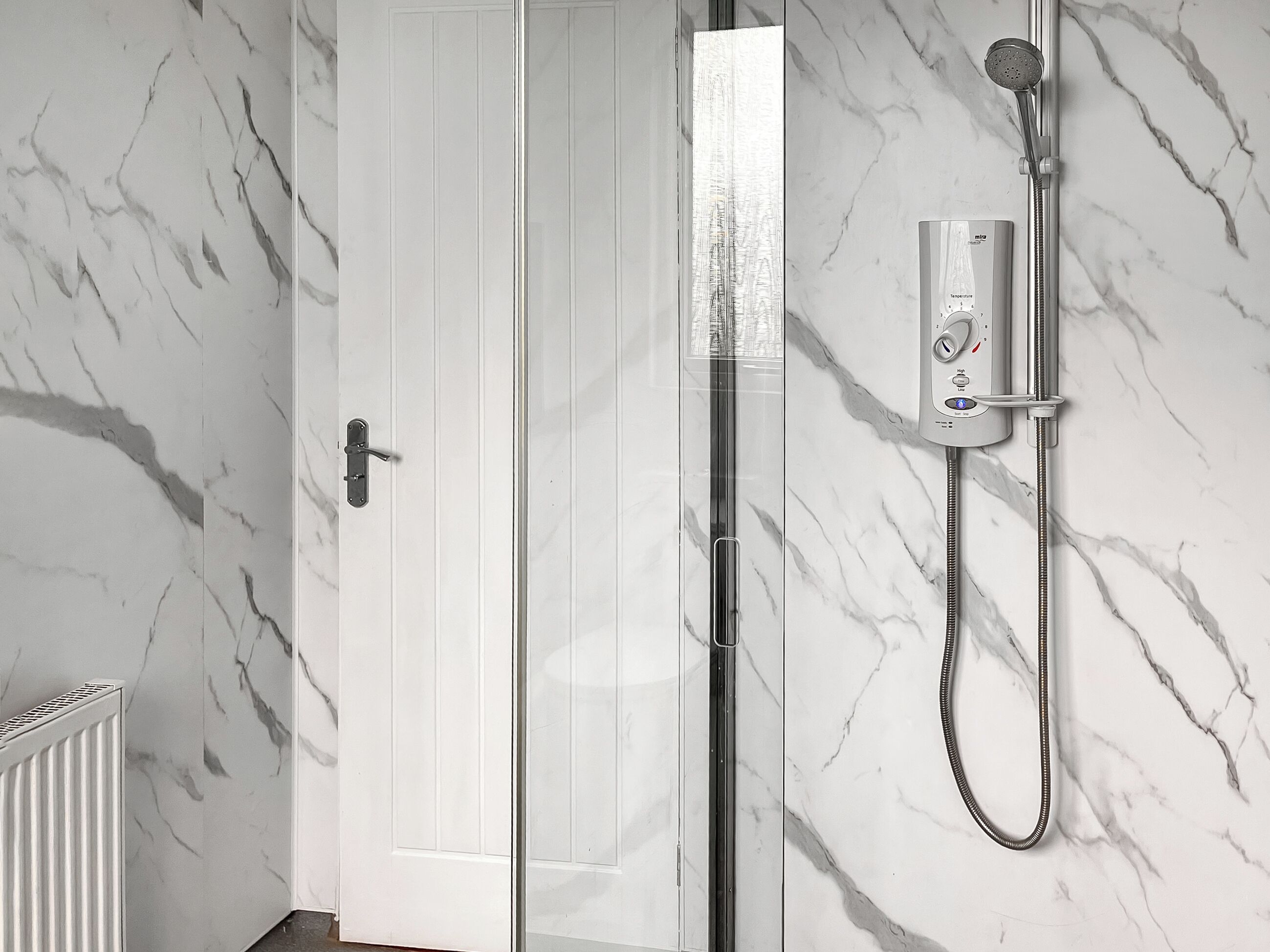 A bathroom with a shower, a white door, and marble walls.