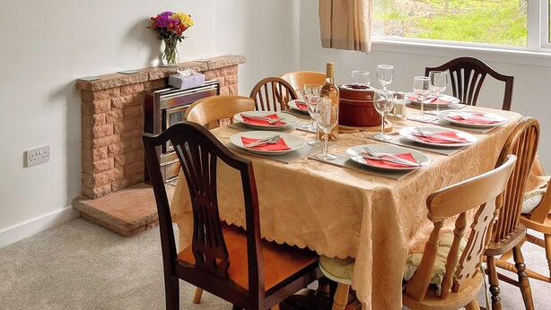 A dining room with a table set for four, chairs, a fireplace, and a window with a view of greenery. - Providing the perfect mix of countryside tranquillity and coastal adventure. (Pinwherry, near Girvan)