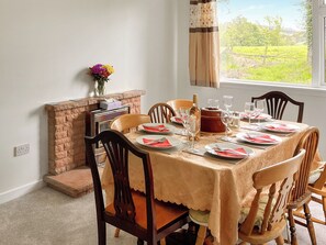 A dining room with a table set for four, chairs, a fireplace, and a window with a view of greenery.