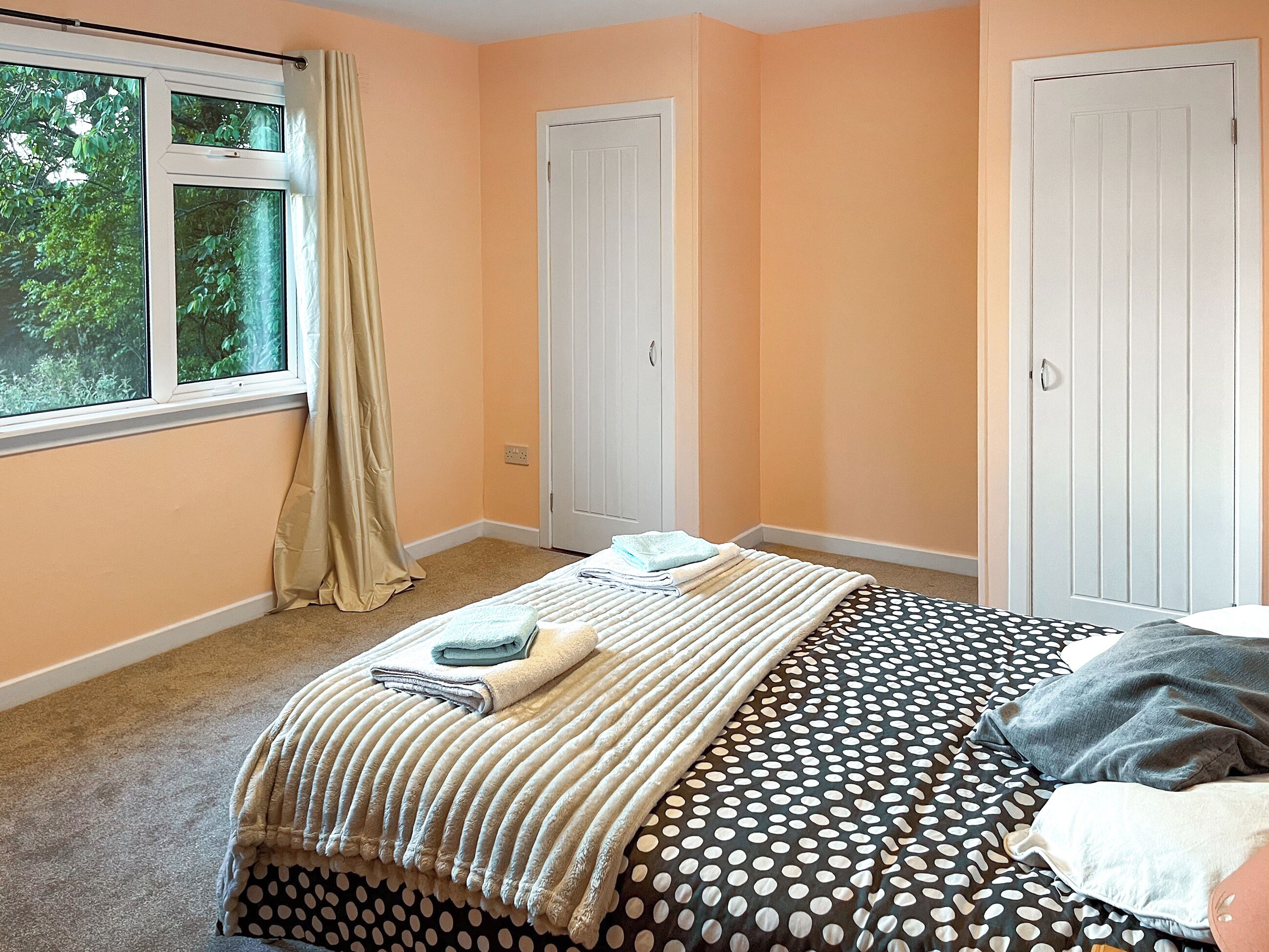 Ein Schlafzimmer mit einem Bett, zwei Türen, einem Vorhangfenster und Teppichboden.