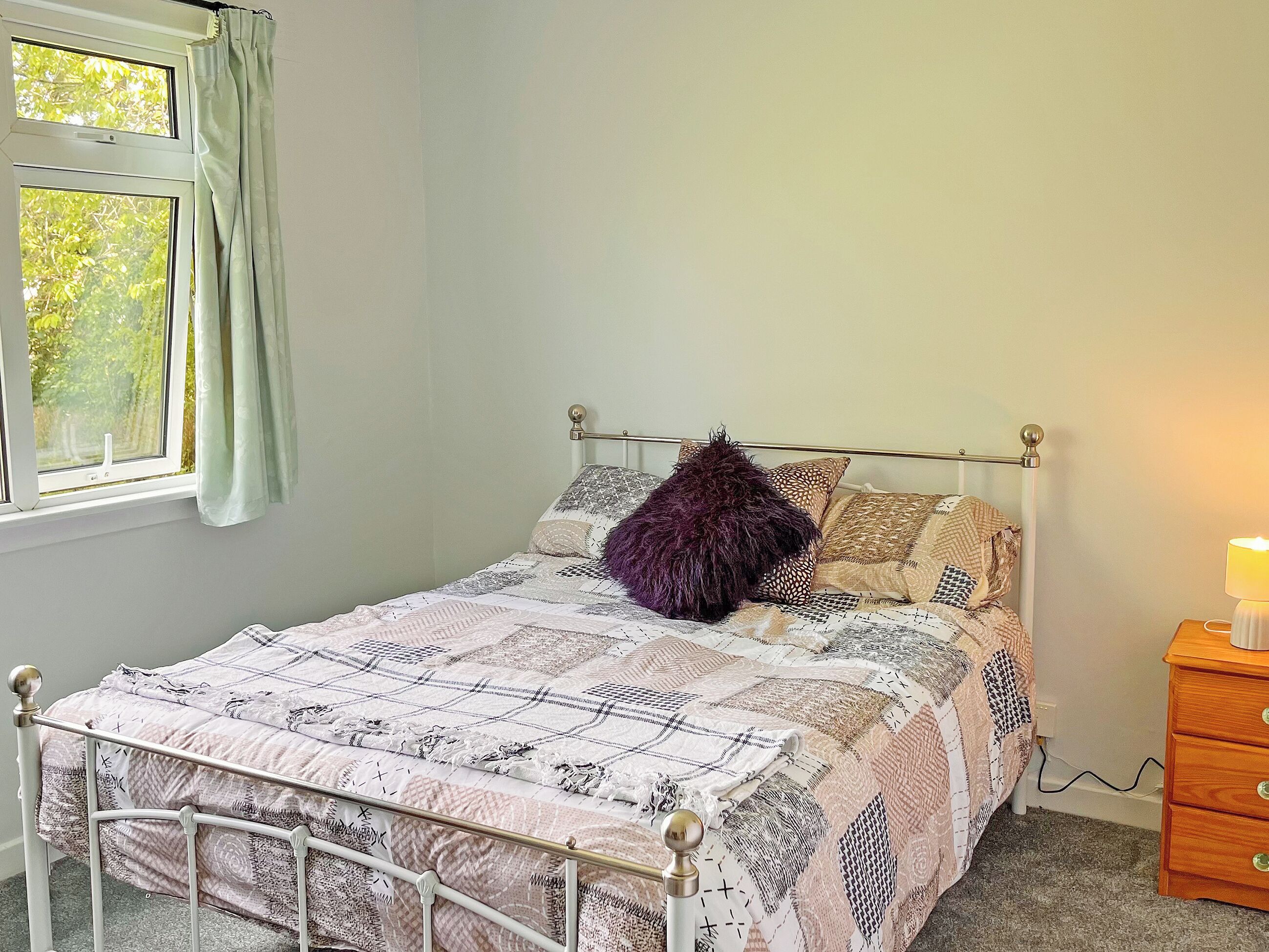 Een slaapkamer met een bed, een raam met gordijnen, een nachtkastje met een lamp en een kledingkast.