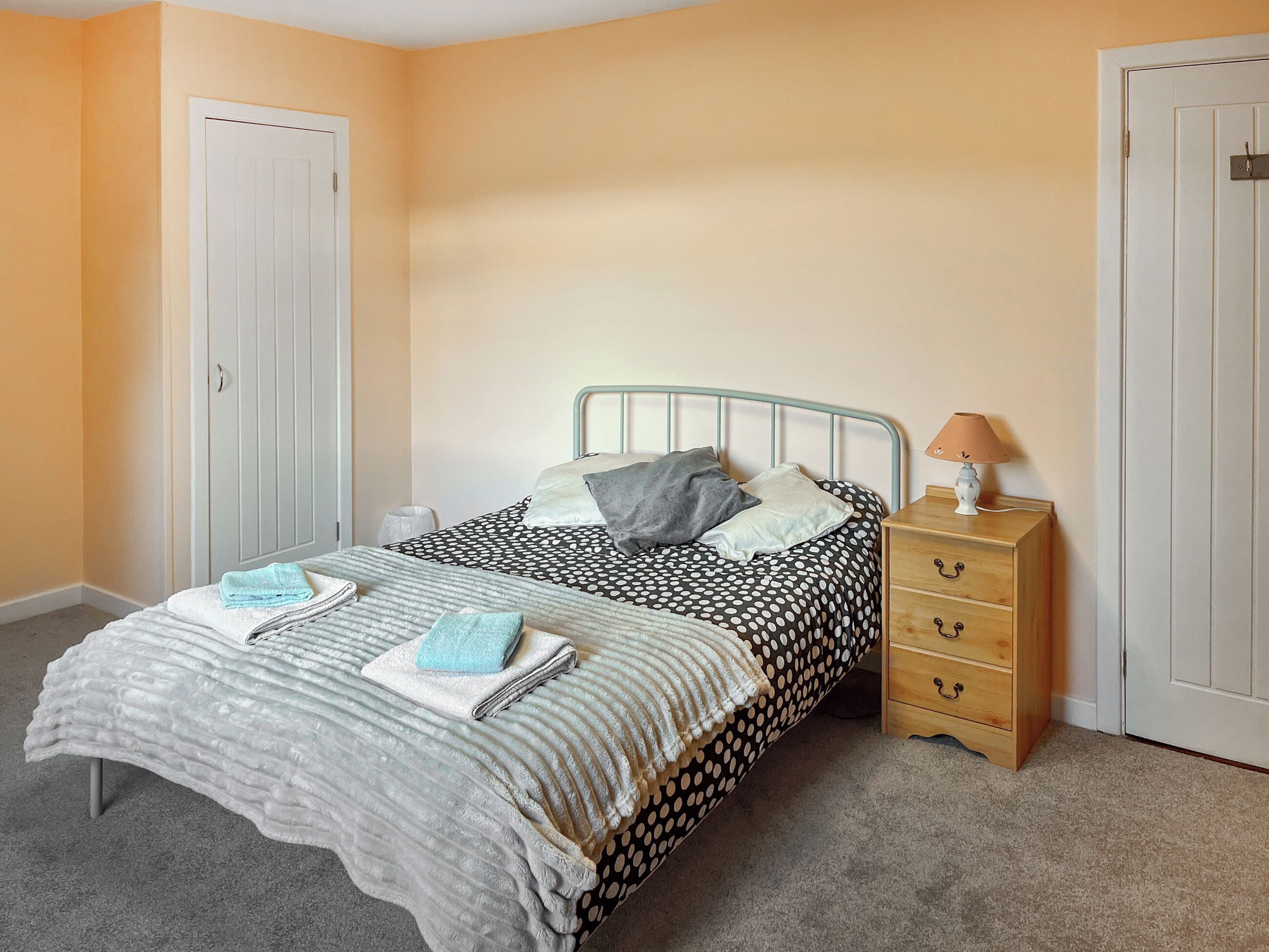 A bedroom with a bed, a nightstand, a lamp, and a dresser.