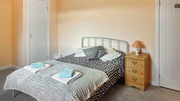 A bedroom with a bed, a nightstand, a lamp, and a dresser.
