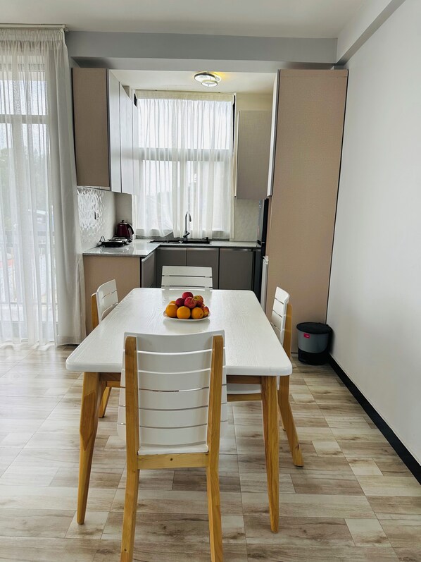 A modern kitchen with white cabinets, a dining table with chairs, and a fruit bowl.