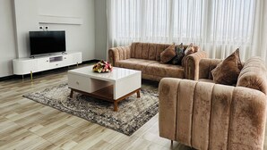 Una sala de estar moderna con un sofá beige, una mesa de centro blanca y un televisor de pantalla plana sobre un mueble blanco.