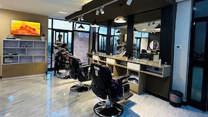 Un salón de belleza moderno con dos sillas de peluquería negras, un mostrador de recepción y un amplio ventanal con vistas a la ciudad.