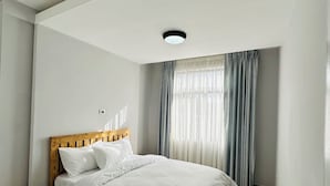 Un dormitorio con cama de madera, ropa de cama blanca, una mesita de noche pequeña y una ventana con cortinas.